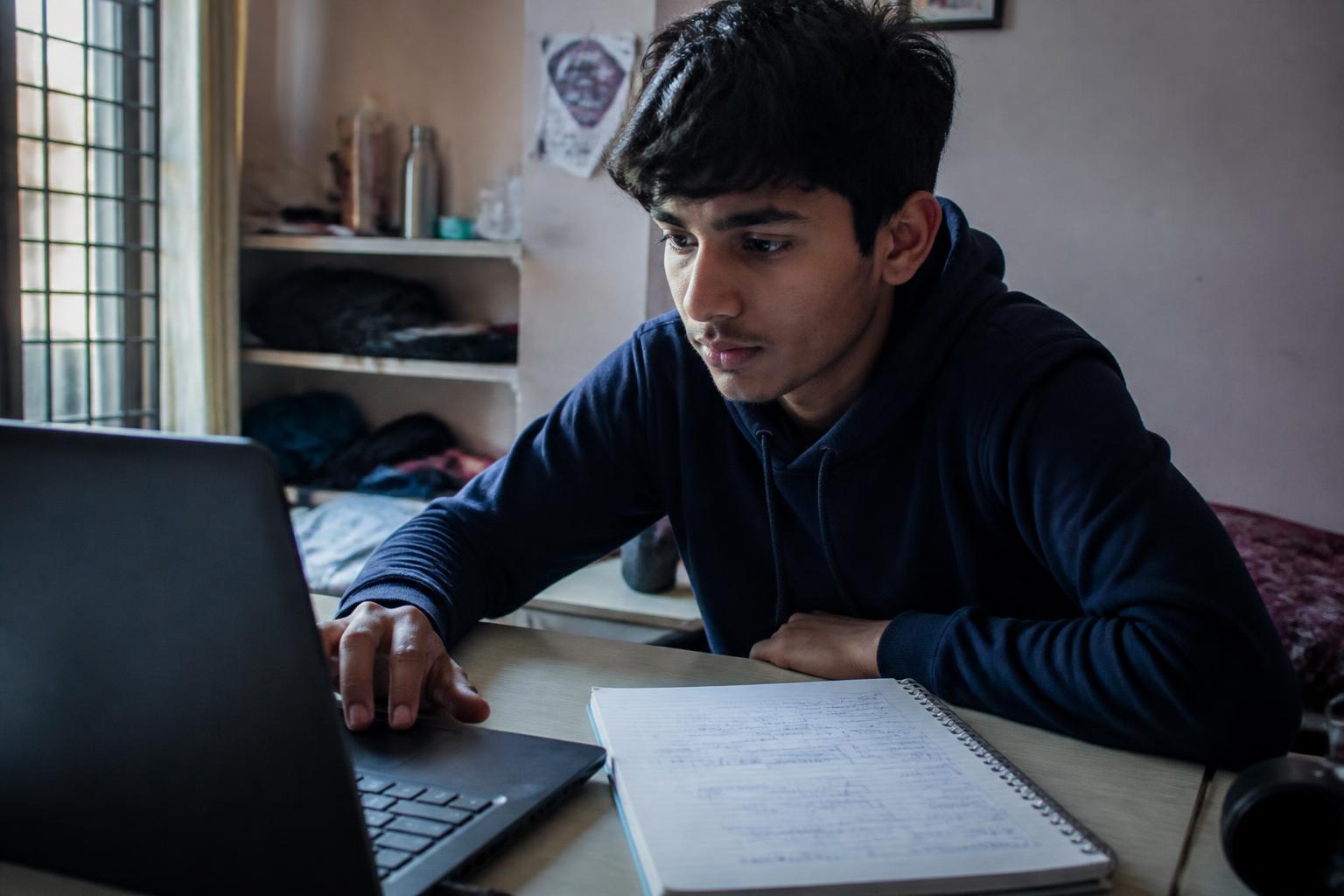 Teen student working through an online digital-skills lesson at a laptop with handwritten notes beside it